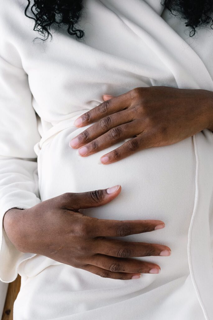 Image of pregnant person holding her belly wearing a white shirt