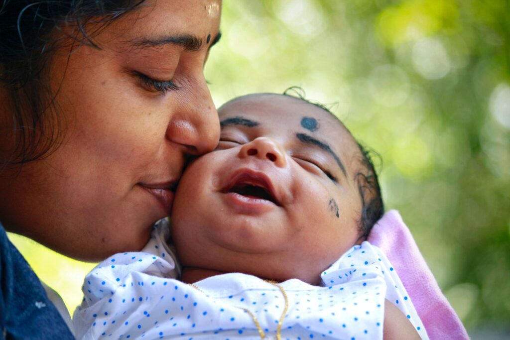 Photo of new parenting and smiling infant in front of trees. 