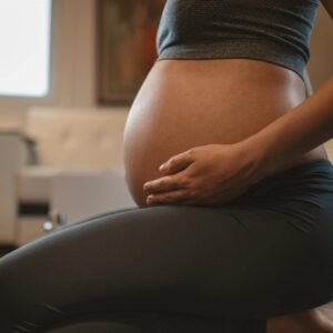 Photo of pregnant person holding their belly, getting ready for a fertility massage. 