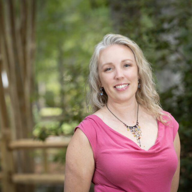 Photo of Justin Robinson, massage therapist, standing outside wearing a pink dress.