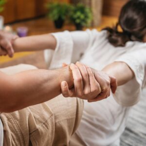 Photo of a woman on a mat with her arms being stretch during a Thai Massage Session,